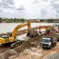 Heavy excavation machinery clearing a wide civic drainage canal in an urban area under the supervision of municipal infrastructure engineers.