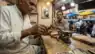 Candid smartphone photo of a jeweler testing a gold coin inside a traditional Indian shop.