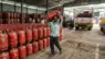 A delivery person lifting a red LPG cylinder at a crowded gas agency warehouse in India.