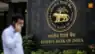 Reserve Bank of India logo on building wall with blurred man talking on phone, finance news concept.