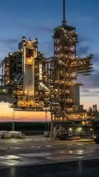 A detailed rocket stands on an illuminated launch pad at dusk against a dramatic sunset sky with a crescent moon representative image