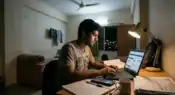 A college student studying late at night in a university hostel room while searching scholarship and financial aid portals on a laptop, symbolizing rising education costs and student financial pressure in India.