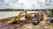 Heavy excavation machinery clearing a wide civic drainage canal in an urban area under the supervision of municipal infrastructure engineers.